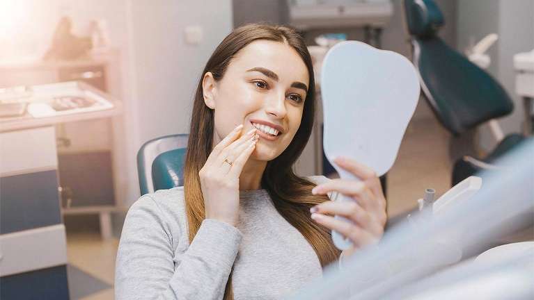 woman sitting in a dental chair while holding a mirror